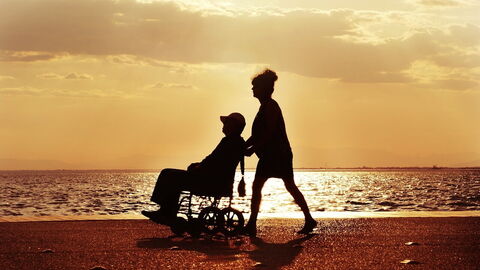 A gentleman in a wheelchair being pushed by a woman on a beach